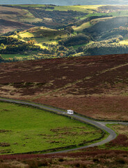 A caravan driving down a single windy road with rolling hills in the background