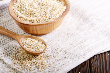 Raw organic superfood gluten free quinoa seeds in wooden spoon and bowl on kitchen table closeup