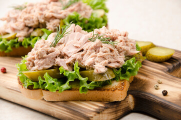 Homemade tuna salad sandwiches on cutting board with pickles aside