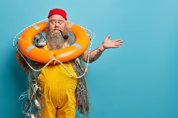 Horizontal shot of shocked embarrassed bearded male seafarer poses with inflated lifering fishing...
