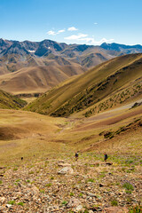 Group of trekkers descending rocky pass with mountain top wiews in high mountains. Young men and women hiking near Sary Chelek lake, Sary-Chelek Jalal Abad region, Kyrgyzstan, Trekking in Central Asia