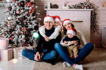 Obraz na płótnie Canvas beautiful relatives at home, charming girl with mom and dad, in red santa claus hat, decorated Christmas tree with lights at home by the fireplace.celebrate, holiday.