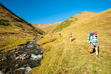 Group of young hikers trekking in mountains. Two women two men backpacking in summer near Sary Chelek lake, Sary-Chelek Jalal Abad region, Kyrgyzstan, Trekking in Central Asia.