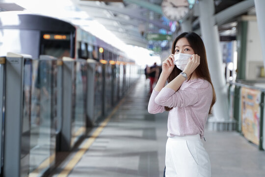 Asian business woman in casual dress code wearing face mask. She is waiting for the train to go to work on the platform station. New normal lifestyle in city concept.
