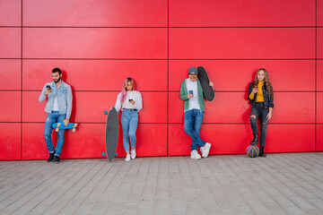 Group of young friends stare at their cell phones while standing against a wall in the city - Teneegers using smart mobile phones
