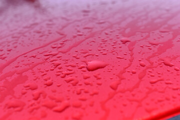 The surface and glass of the red car covered with raindrops