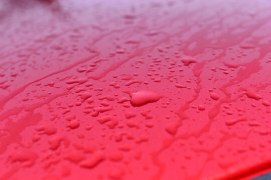 The surface and glass of the red car covered with raindrops