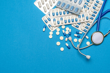 Health care or illness concept - stethoscope and pills on blue background