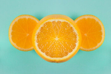Bright orange pulp cut with two slices on the sides, forming an elegant geometric composition on a blue paper texture background. Creative cooking and healthy food.