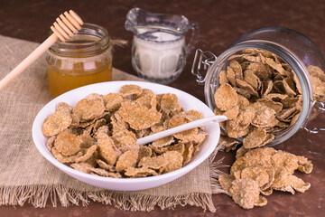 Whole grain breakfast cereals with honey and nuts in a plate on a brown background.