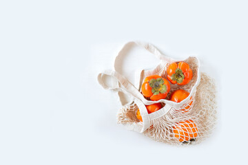 Ripe orange persimmon in a mesh shopping bag on a white background. Copy space for text.