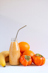 Glass bottle with smoothie, persimmon, banana and orange drink on a white background. Copy space. Raw, vegan food. Banner.