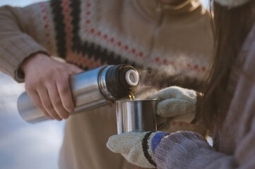A man pours a hot drink from a thermos into a cup for a woman.