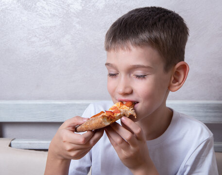 Cute Boy Eating A Slice Of Pepperoni And Cheese Pizza, The Child Closed His Eyes In Pleasure, Close-up, Copy Space