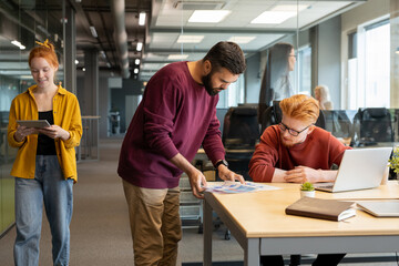 Young bearded businessman showing his colleague some financial papers