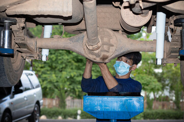 Mechanician changing car wheel in auto repair shop wearing a mask, coronavirus concept