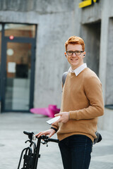 Smiling handsome young man with ebike and phone on the street.