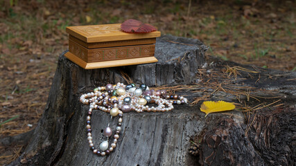 Pearl necklaces and an old carved wooden jewelry box stand on a cracked stump.