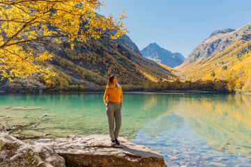 Happy woman at crystal lake in the autumnal mountains. Mountain lake and traveller girl
