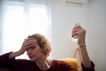 Woman with headache using aircondition unit at home.