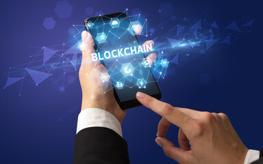 Female hand holding smartphone with BLOCKCHAIN inscription, modern technology concept