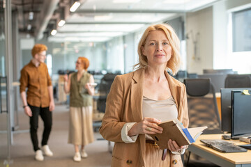 Successful mature blond businesswoman with open notebook looking through notes