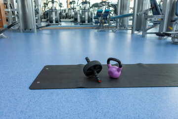 Sports and fitness equipment. Kettlebell and ab roller on mat in gym