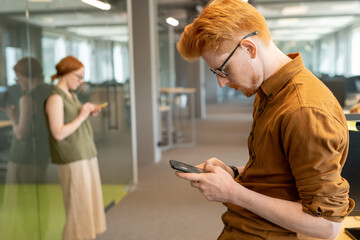 Young serious businessman scrolling through contacts against his colleague