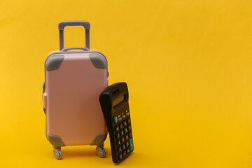 Travel expenses. Mini pink plastic travel suitcase with calculator on yellow background. Minimal...
