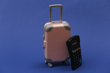 Travel expenses. Mini plastic travel suitcase with calculator on classic blue background.