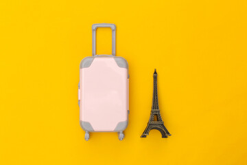 Traveled to Paris. Mini plastic travel suitcase and statuette of the Eiffel Tower on yellow background. Top view. Flat lay