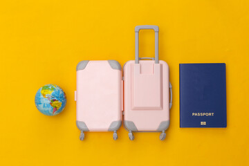 Travel flat lay. Mini plastic travel suitcase, globe and passport on yellow background. Minimal style. Top view