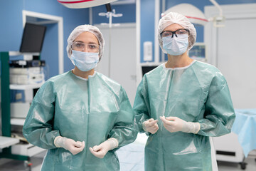 Two young professional female surgeons in protective uniform, gloves, mask, etc