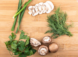 Top view. Chopped and whole mushrooms, green onions, parsley and dill on a wooden background with space for text.
