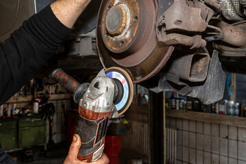 A mechanic grinds, with an angle grinder, the edge of an old rear brake disc in a car, regeneration...