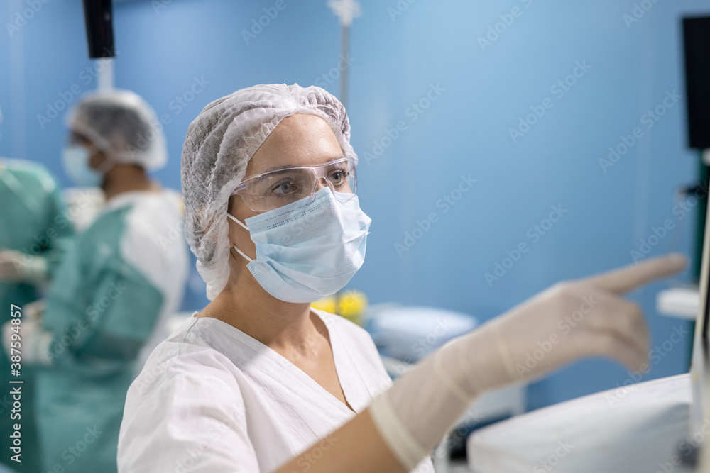 Poster young assistant of surgeon in gloves, mask and uniform pointing at display