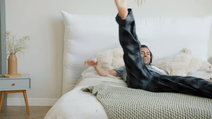 Happy mixed race guy in pajamas is running to bed jumping relaxing enjoying rest at home in bedroom. Joyful youth and modern lifestyle concept. - Powered by Adobe
