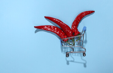 Shopping cart with hot red chili peppers on blue bright background