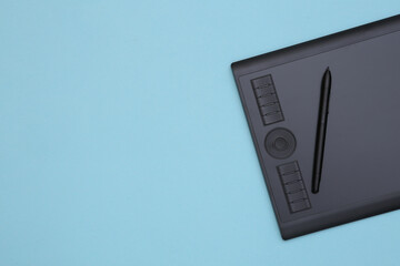 Graphic tablet with pen on blue background. Top view. Copy space