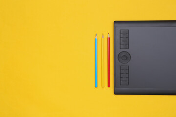 Graphic tablet and colored pencils on yellow background. Top view