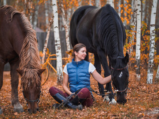 Two female riders sit on the grass next to the horses