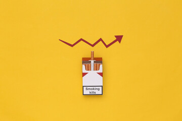 Fototapeta na wymiar Pack of cigarettes and a growth arrow on yellow background.