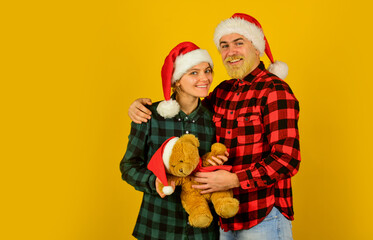 Fototapeta premium Family santa hats. Entertainment ideas for adults. Family holiday. Loving couple yellow background. Christmas time. We love christmas. Couple in love with teddy bear soft toy enjoy christmas holiday