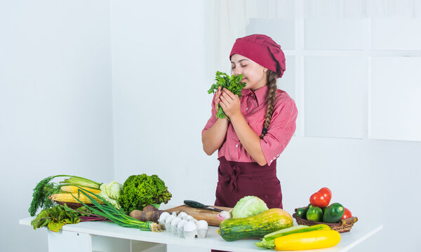 Smells Good. Teen Girl Smell Parsley. Fresh Raw Vegetables. Time To Eat. Happy Child Cooking In Kitchen. Healthy And Organic Food Only. Full Of Vitamins. Kid Wear Chef Uniform And Hat