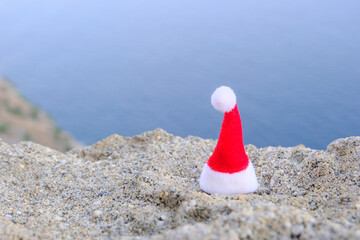 Red Santa Claus cap on a cliff with sea view. The concept of a hat for the holiday. A beautiful hat is a symbol of the coming year.