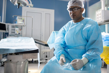 Tired professional male surgeon in protective workwear sitting in operating room