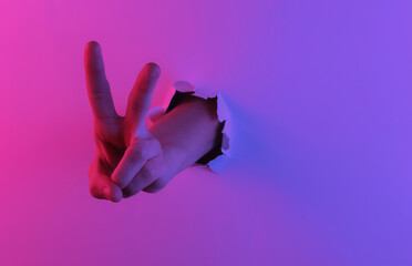 Mystical halloween concept. Hand shows V gesture through a torn hole..Creative pop art pink blue...