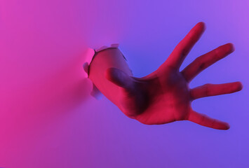 Mystical halloween concept. Hand through a torn hole. Creative pop art pink blue neon color. Trendy gradient illumination. Night light