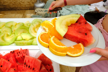 Fruit slices in a plate. A girl holds a plate. Watermelon, melon , oranges . Vitamins, dietary dessert concept.Meals for tourists in hotels and restaurants.