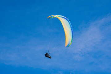 Colourful paraglider flies on a blue sky background. Extreme sport.
